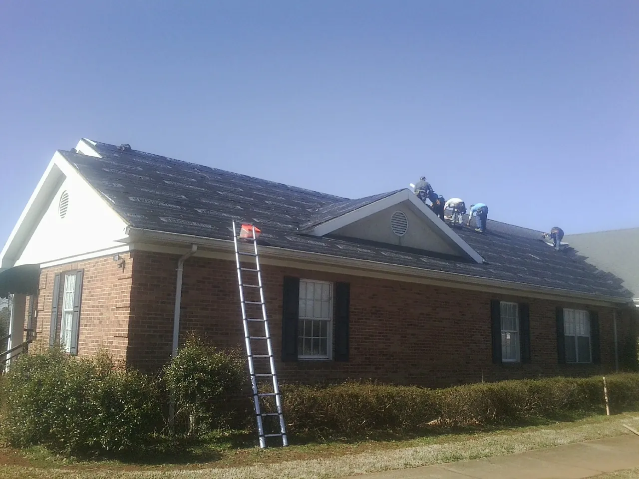 Crew tearing shingles off a brick ranch roof with a ladder set — Emergency Roof Repair work by our crew in Fort Hall