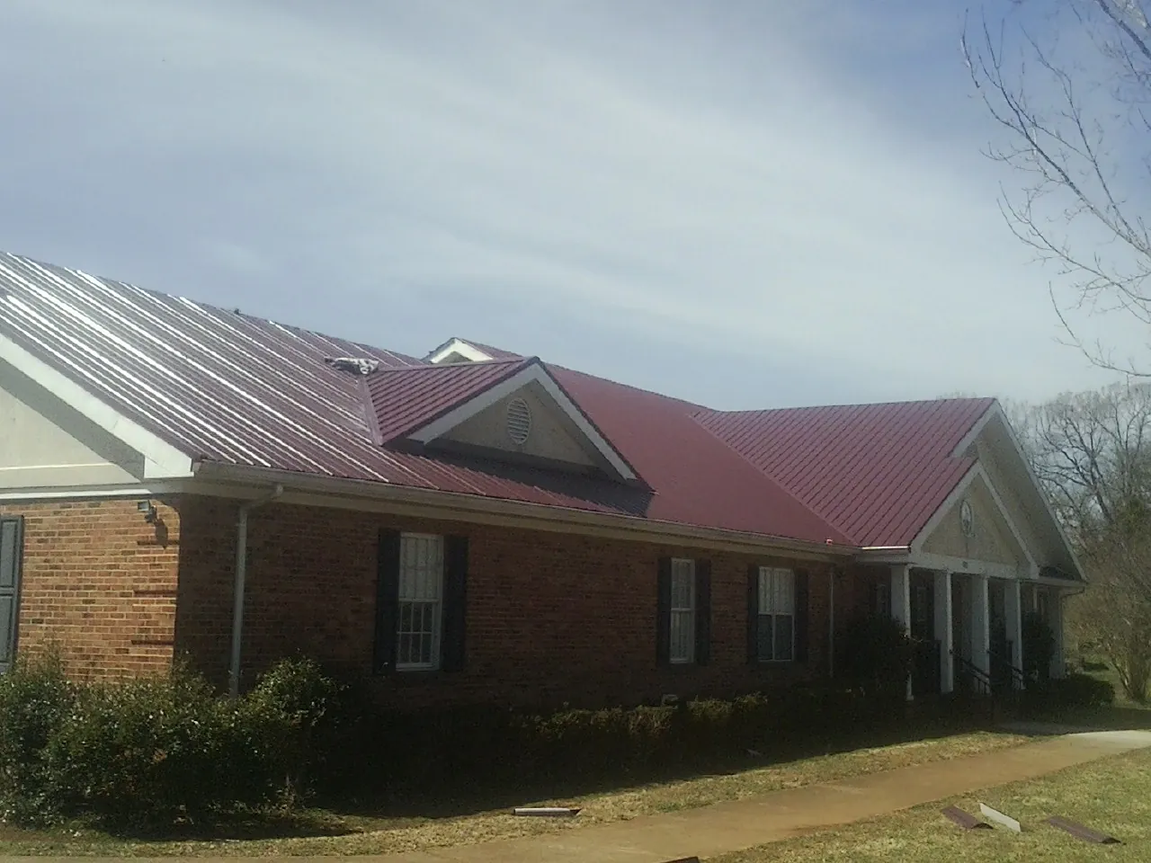 Red metal roof with gabled entries on a long brick building, from a Hail Damage Roof Repair job in Fort Hall
