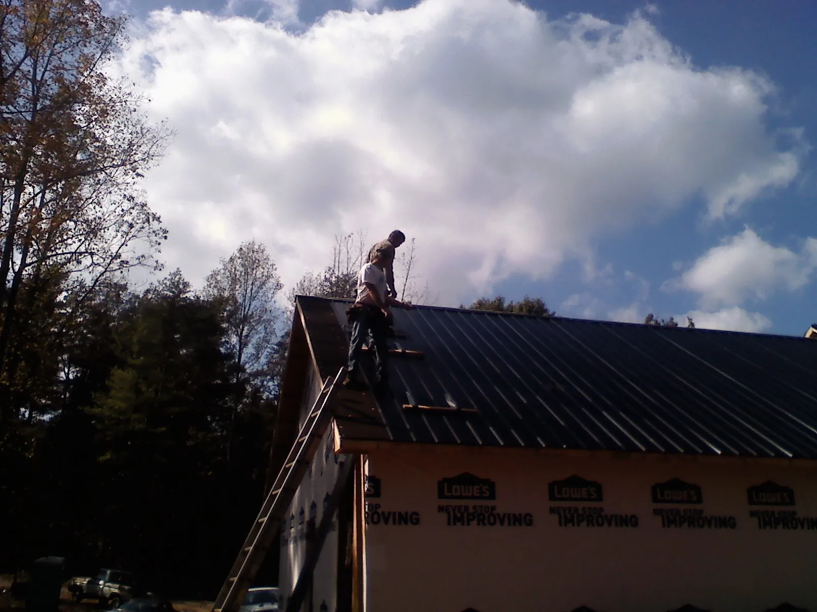 Roofer fastening dark metal panels high against a cloudy sky, from a Roof Inspection job in Fort Hall