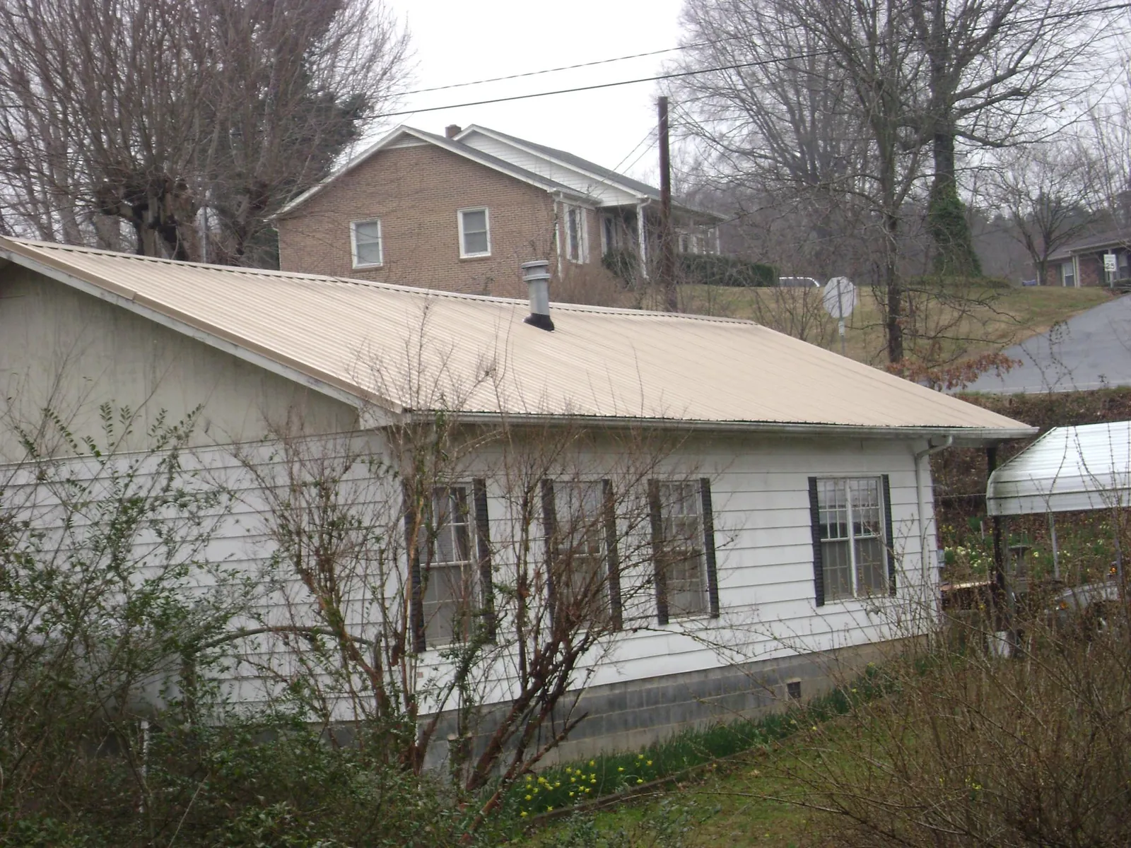 Tan metal roof on a white sided house set into a hillside — Commercial Roofing by Roofing Brothers in Fort Hall